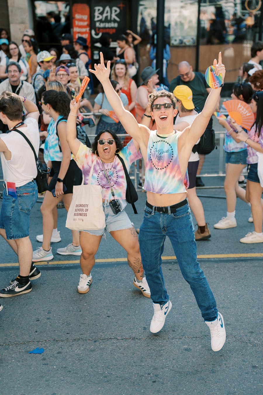 Participants joyfully celebrate at a pride parade, wearing vibrant tie-dye shirts and accessories.