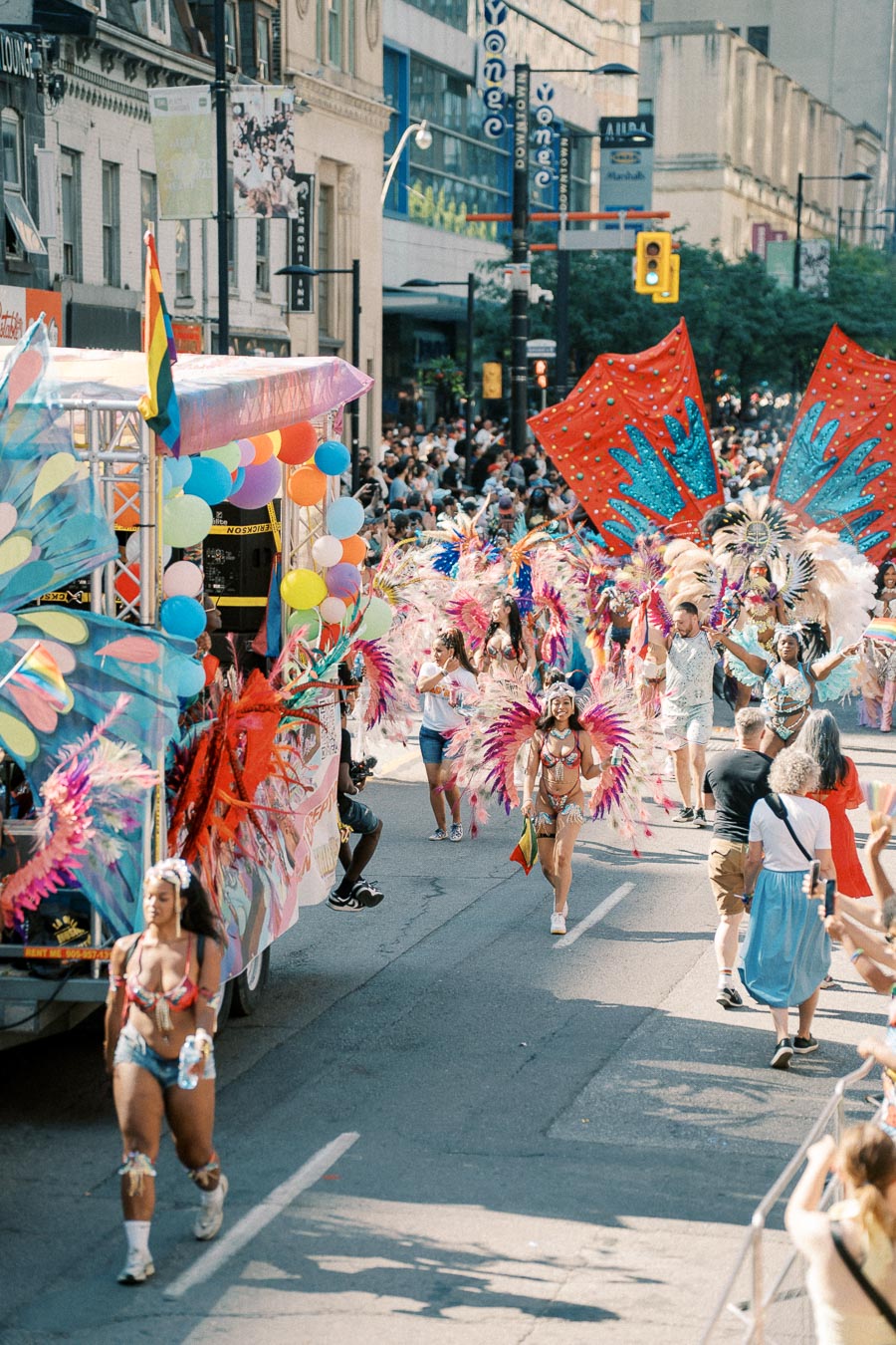 A lively street parade featuring participants in colorful feathered costumes and a float adorned with balloons, capturing the festive atmosphere.