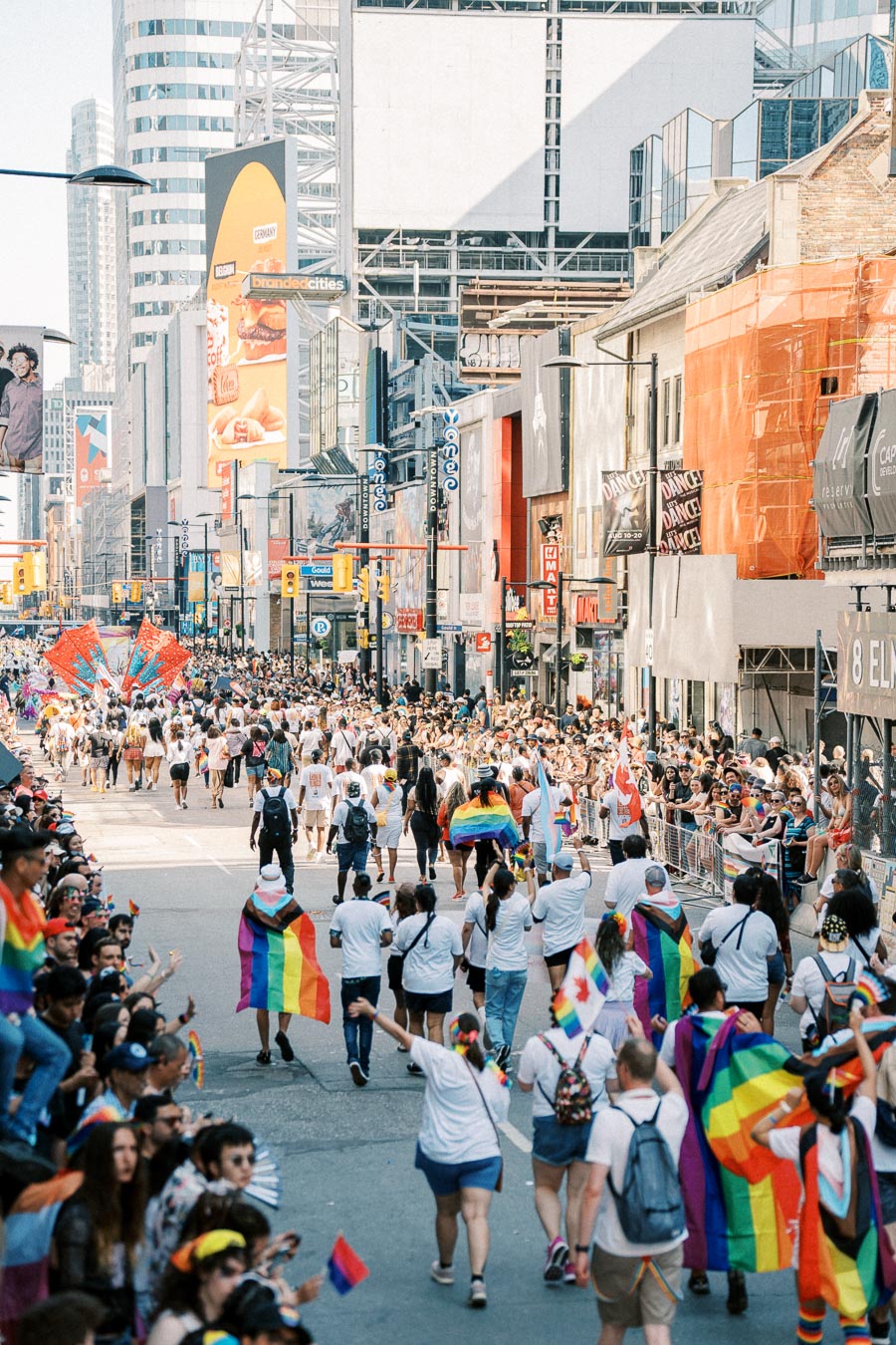 A lively LGBTQ+ pride parade with participants waving rainbow flags and wearing colorful attire, surrounded by cheering crowds in an urban setting.
