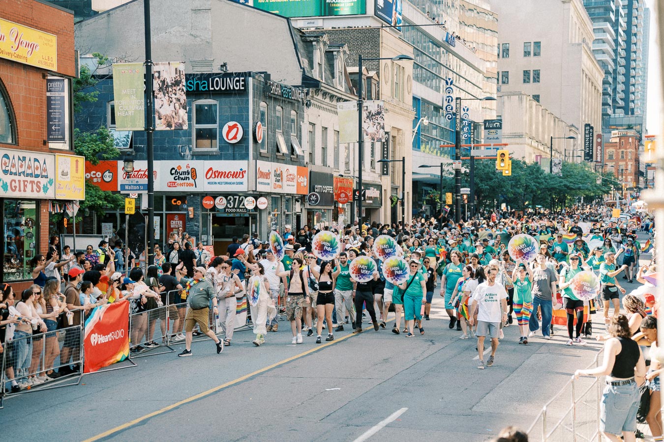 A vibrant parade in Toronto featuring participants with colorful signs and a large crowd of spectators.