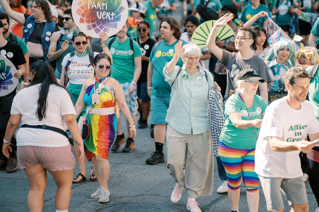 Participants in a parade wearing colorful outfits and holding 'Parti Vert' signs, celebrating diversity and environmental awareness.