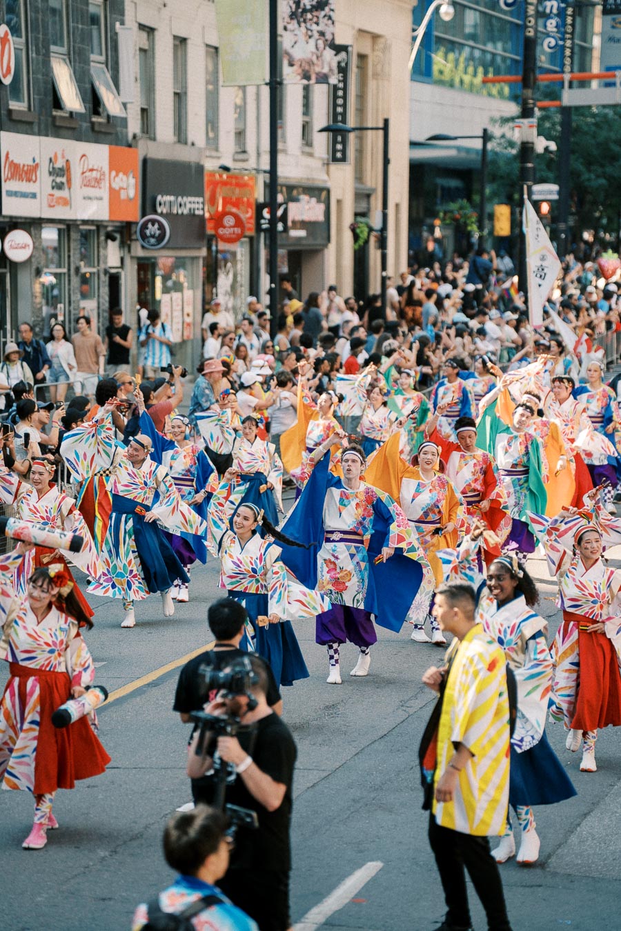 Participants in colorful traditional costumes parade down a city street, surrounded by a crowd of spectators.