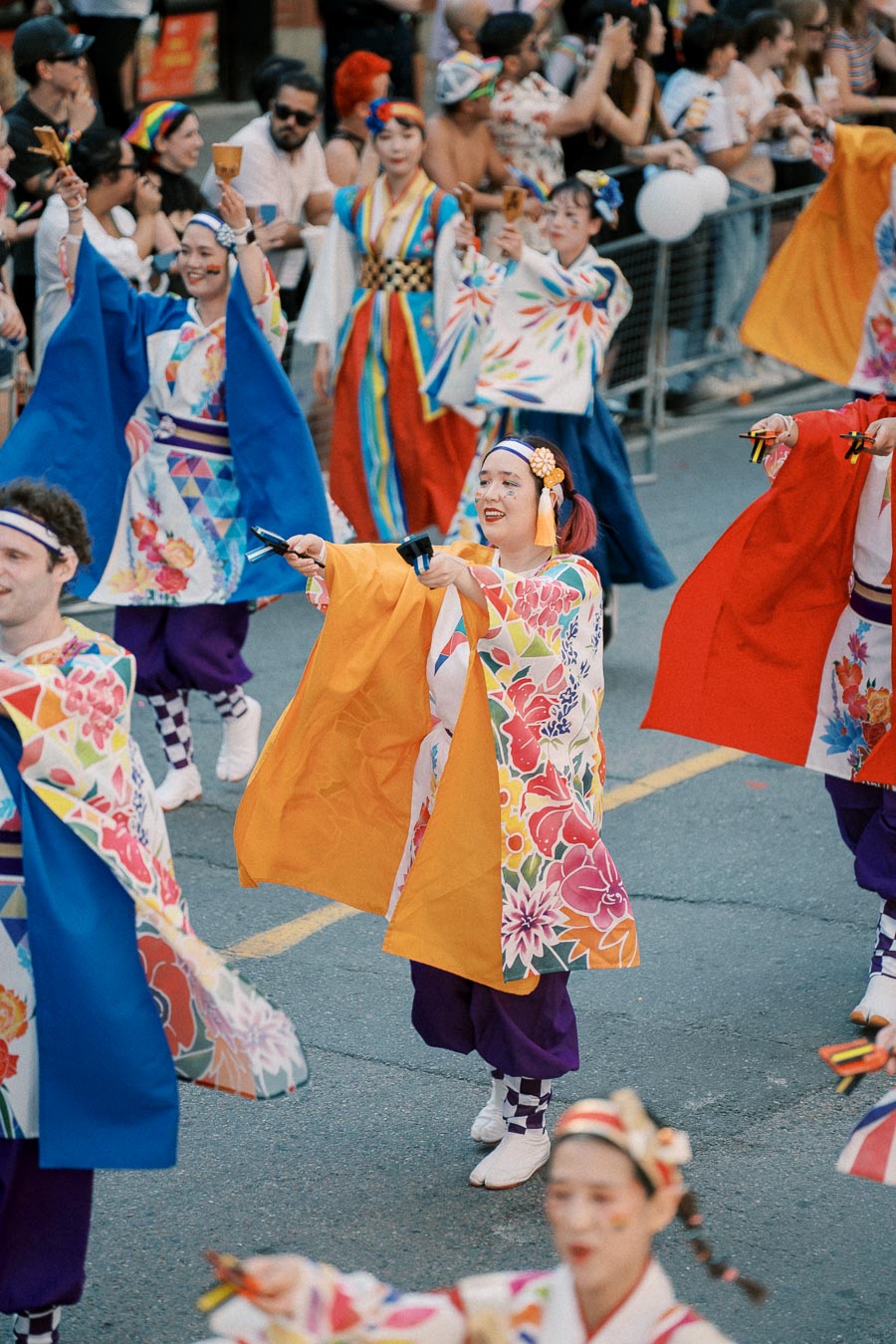 Participants in vibrant traditional Japanese attire perform in a lively parade, showcasing cultural dance and music.