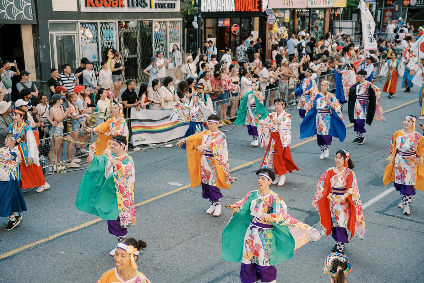 Participants in vibrant traditional costumes perform in a lively street parade, drawing the attention of an enthusiastic crowd.