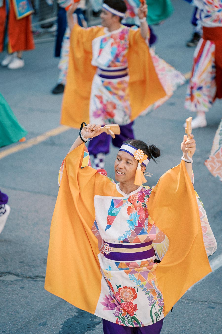 Participants in vibrant traditional costumes perform in a lively street parade, drawing the attention of an enthusiastic crowd.