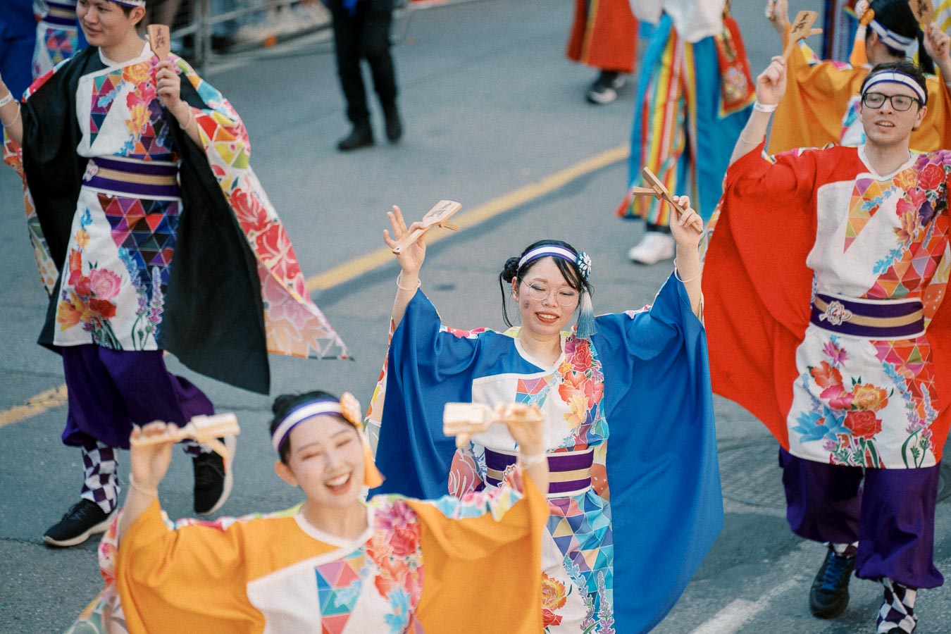 Participants in vibrant traditional Japanese attire perform a dance during a street parade.
