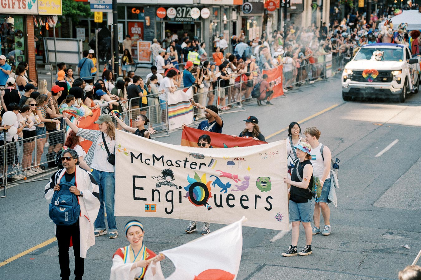 Participants in a parade hold a banner reading 'McMaster EngiQueers', celebrating diversity and inclusion.