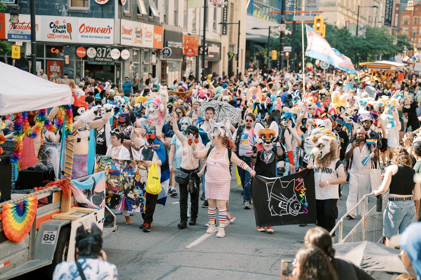 A vibrant parade featuring participants in colorful costumes and animal masks, celebrating diversity and creativity on a bustling city street.