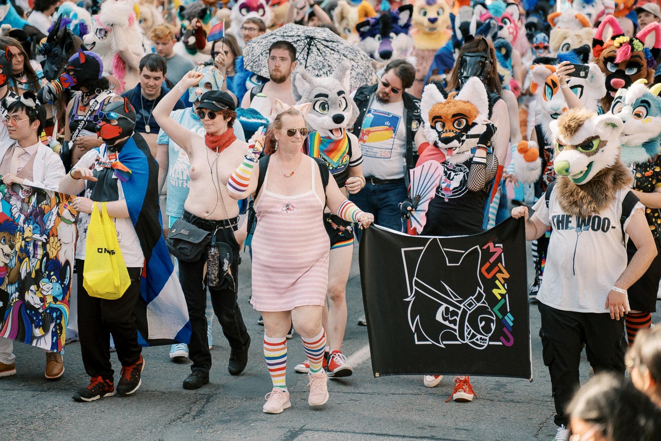 Participants in a vibrant parade, many dressed in colorful costumes and animal masks, celebrate with flags and banners.