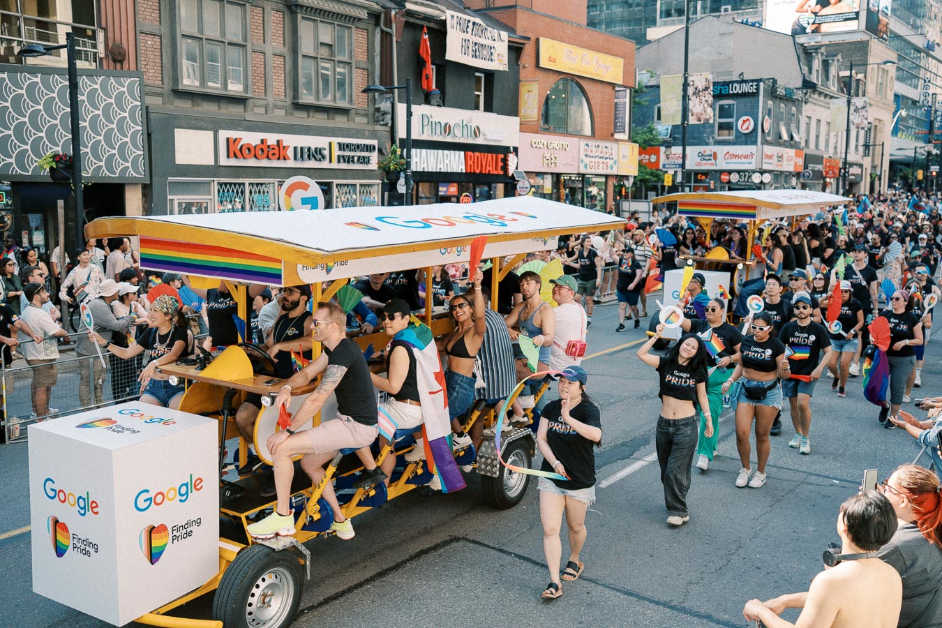 Participants celebrate at a Pride parade with a Google-themed float, showcasing colorful decorations and joyful expressions.