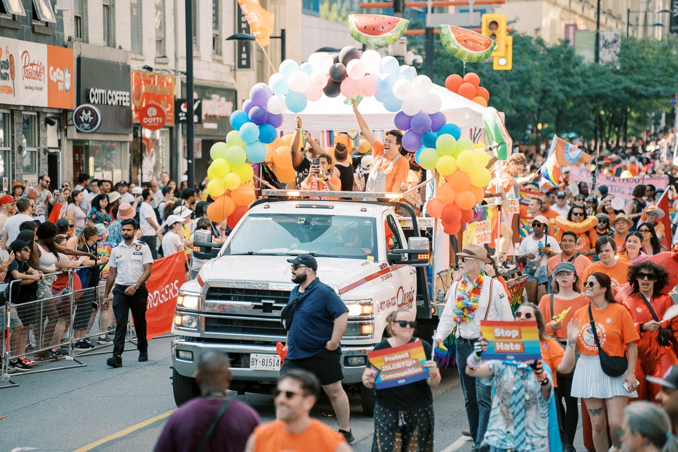 A colorful parade float adorned with rainbow balloons moves through a city street during a lively LGBTQ+ pride parade, with participants and spectators celebrating diversity and inclusion.