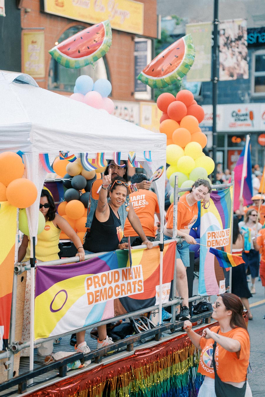 Participants on a colorful parade float celebrate at a pride event, displaying rainbow flags and balloons.