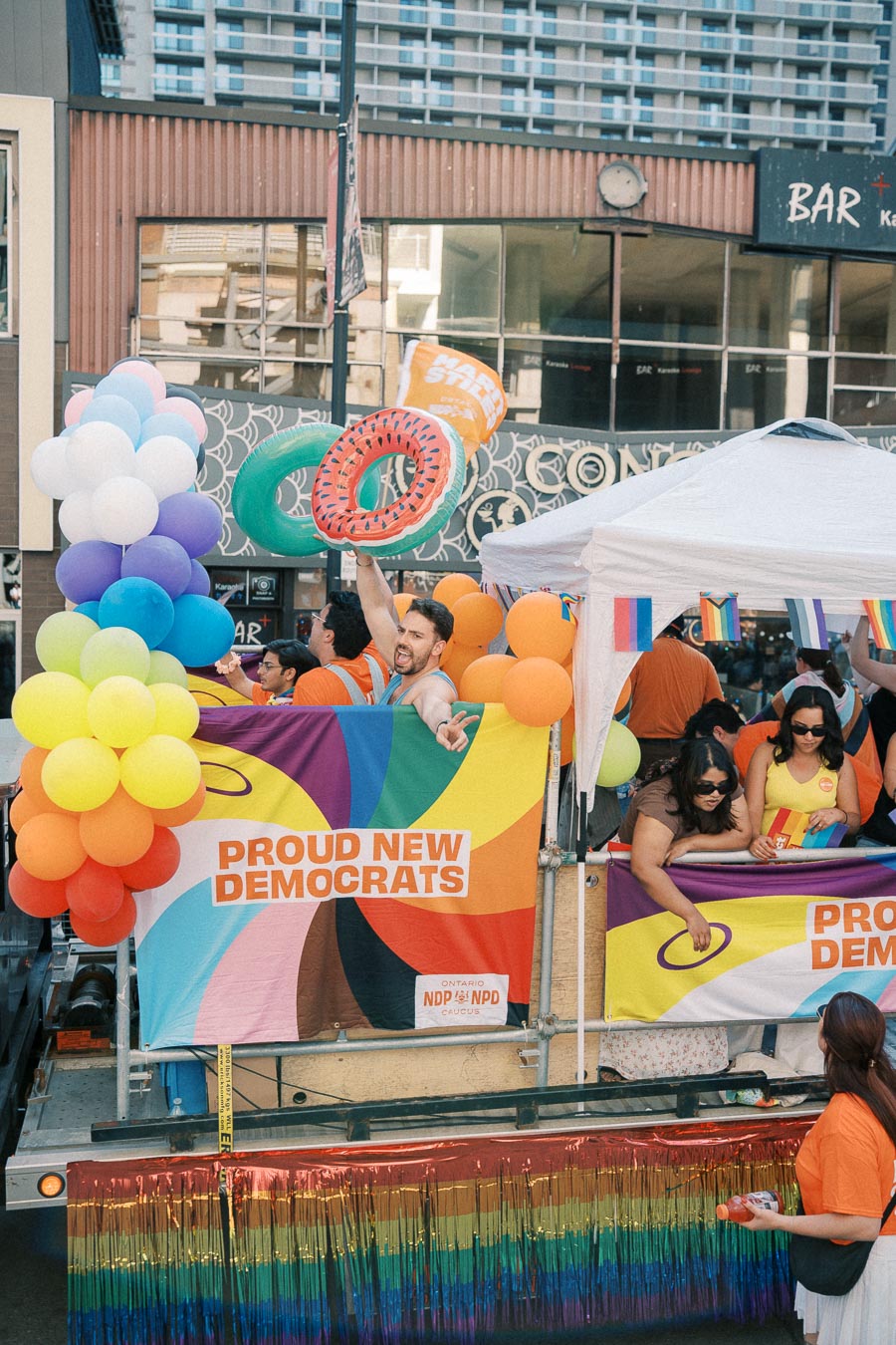 A vibrant parade float featuring rainbow balloons and banners with 'Proud New Democrats', celebrating diversity and inclusion.