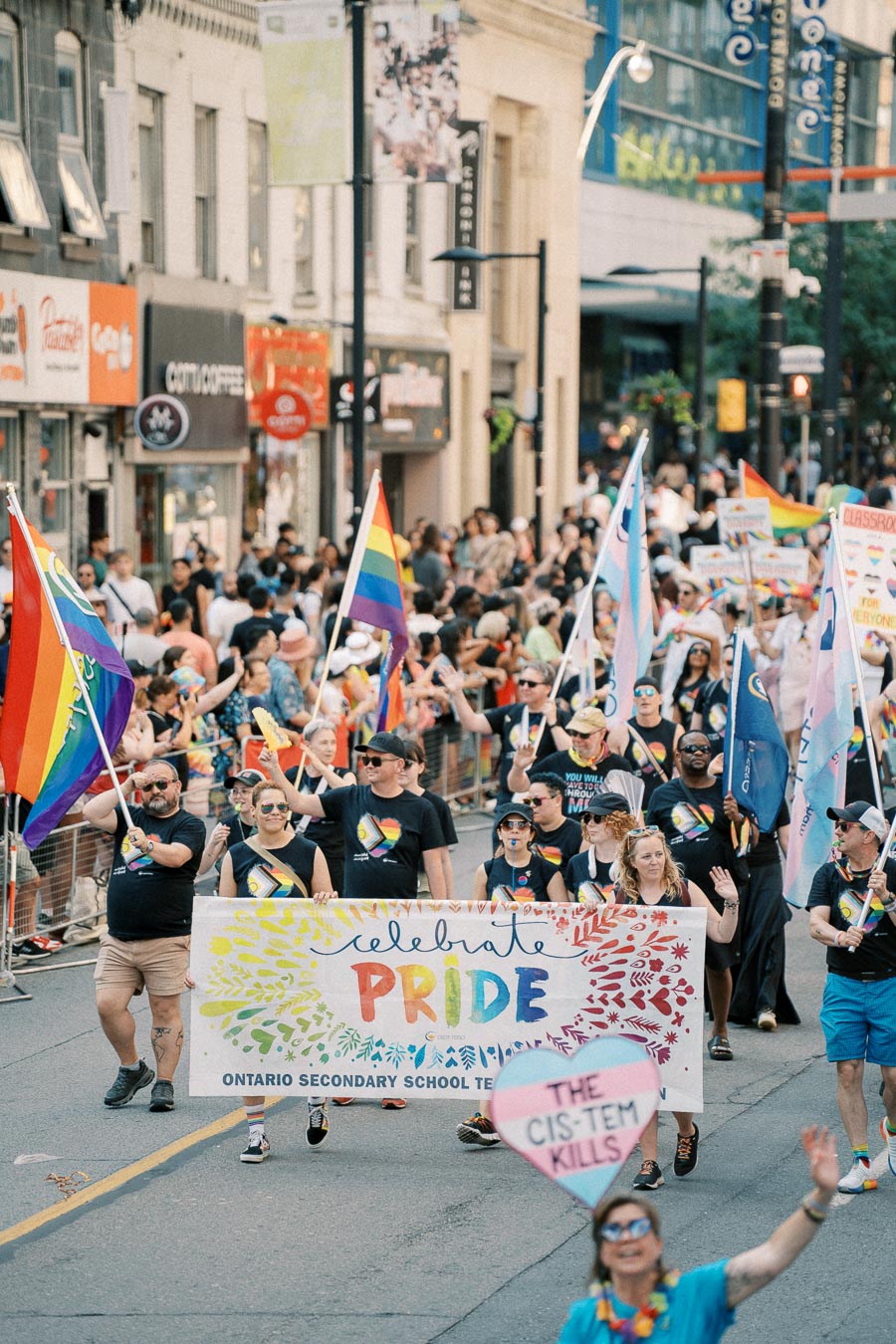 Participants in a Pride parade march with a colorful banner and flags, celebrating diversity and inclusion.