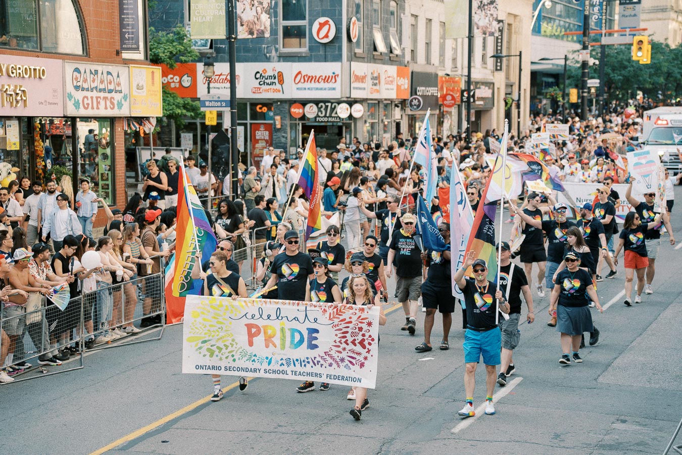 Participants in a pride parade in Toronto march with a banner and rainbow flags, celebrating diversity and inclusion.