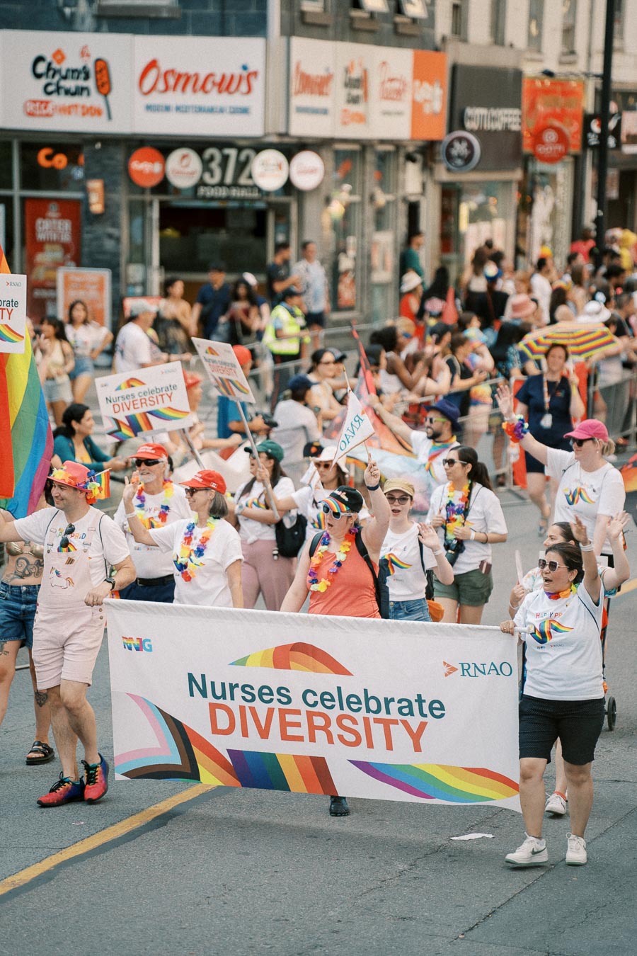Participants in a parade celebrating diversity, with a focus on nurses, hold a colorful banner and wear vibrant attire.