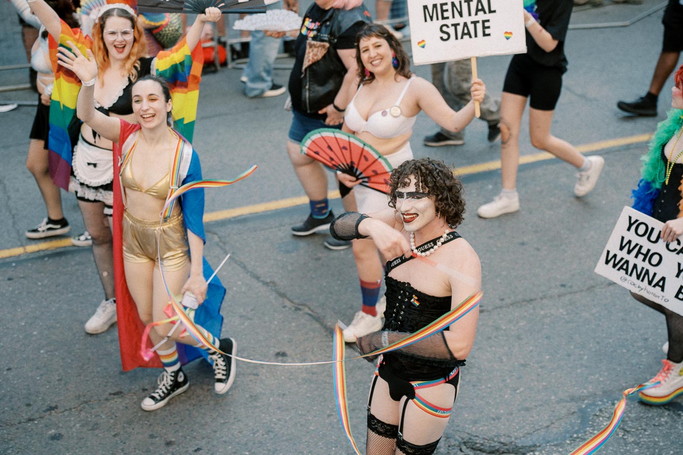 Participants in a pride parade wearing vibrant costumes and holding rainbow flags and signs, celebrating diversity and inclusion.