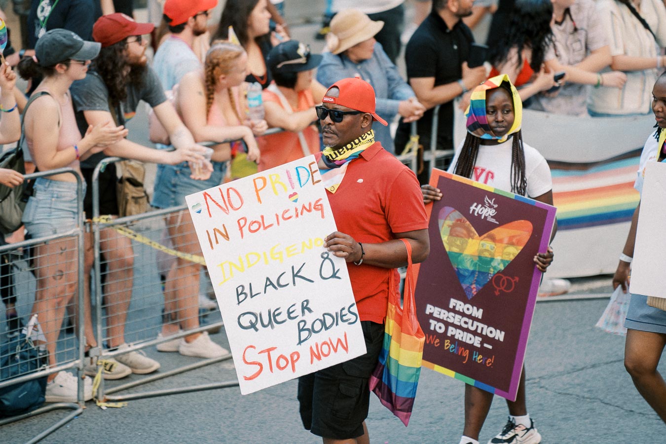 Participants in a pride parade hold signs advocating for Indigenous, Black, and queer rights, emphasizing the message "No Pride in Policing."
