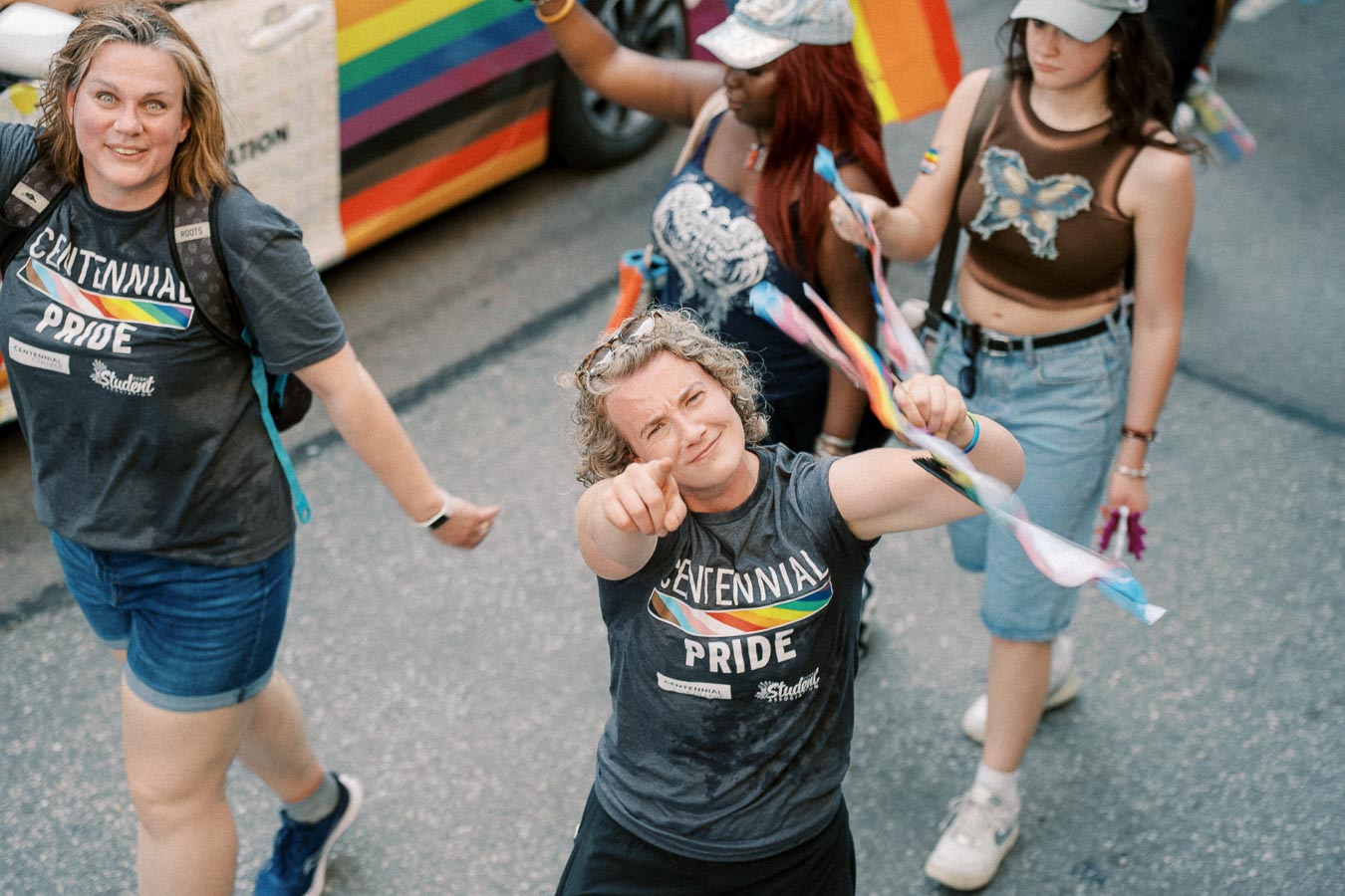 Participants at a pride parade celebrating diversity and inclusion, wearing rainbow-themed attire and waving flags.