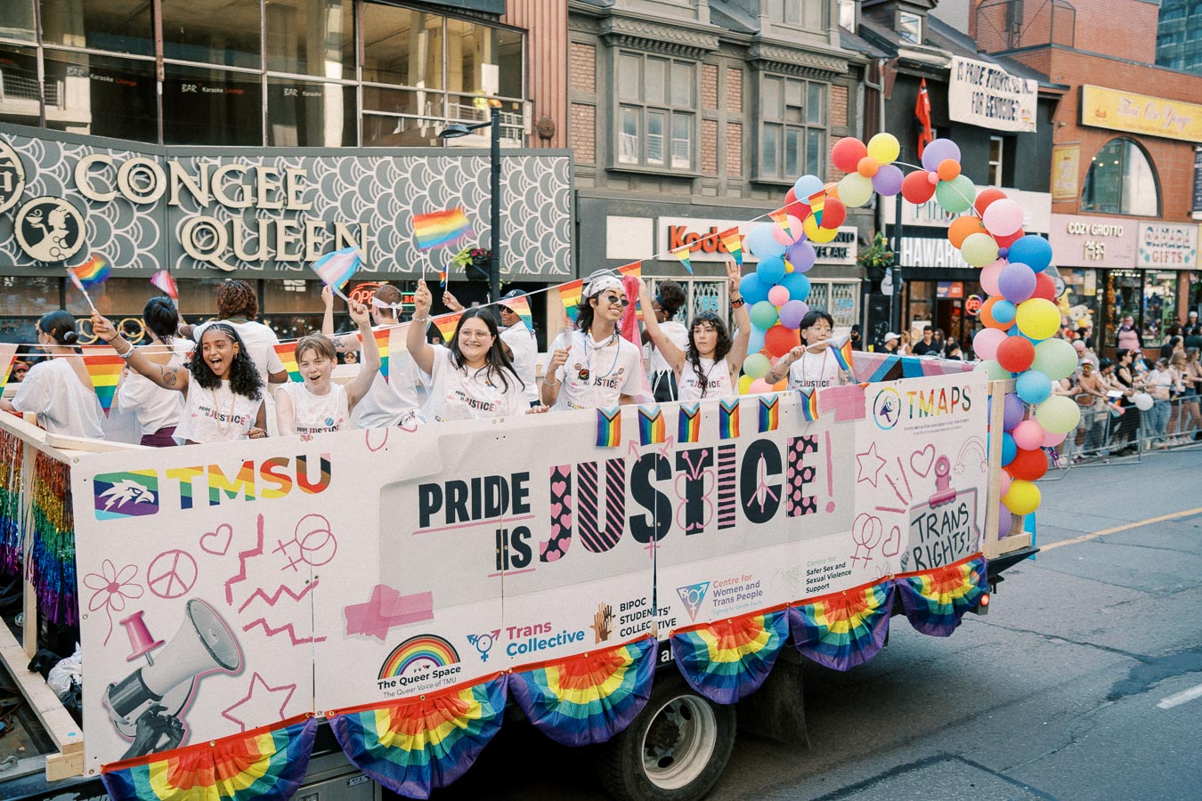 Participants celebrate on a colorful float during a Pride parade, promoting messages of justice and trans rights.