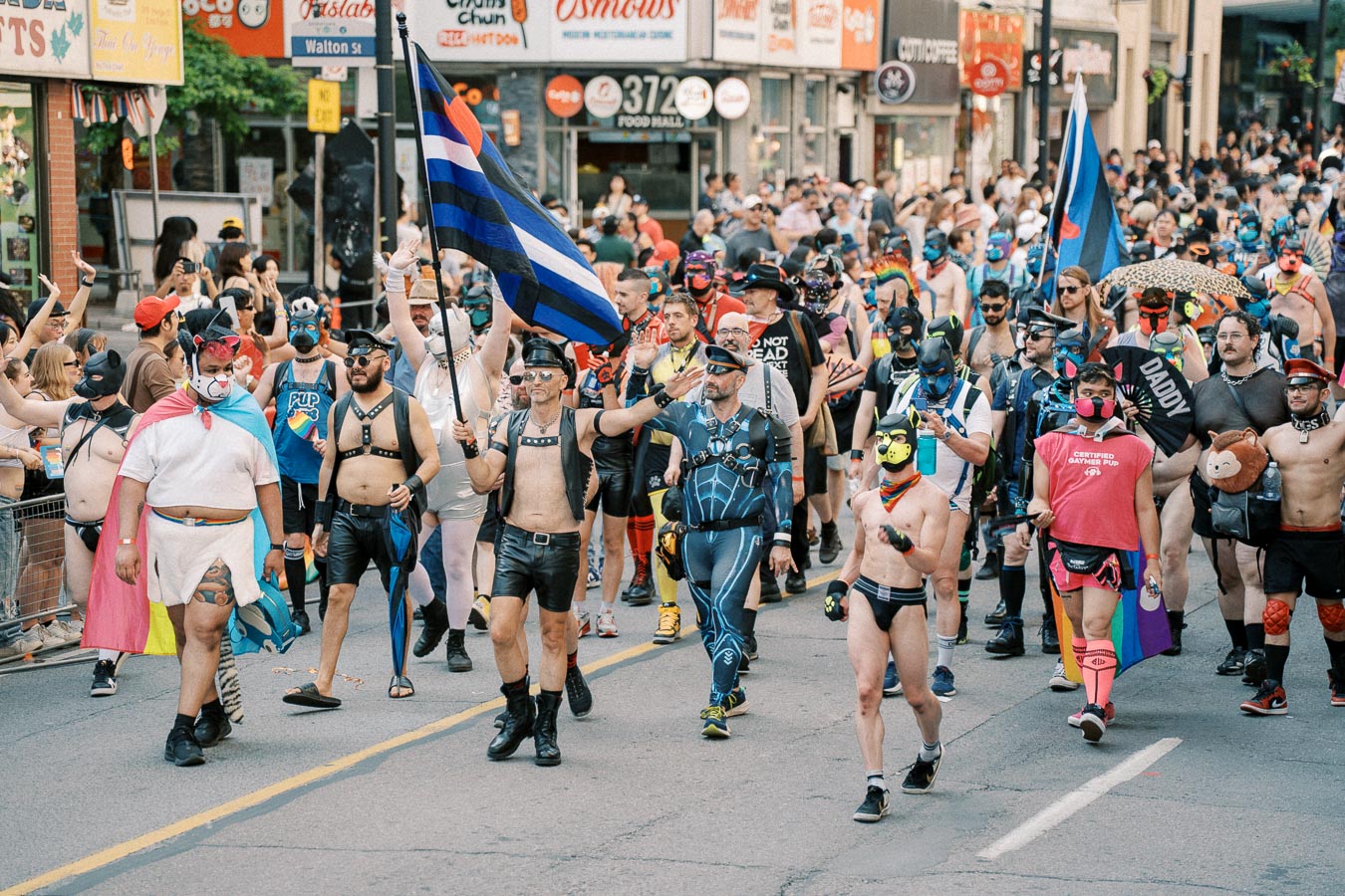 Participants in vibrant costumes march in a lively parade, showcasing diversity and celebration on a bustling city street.