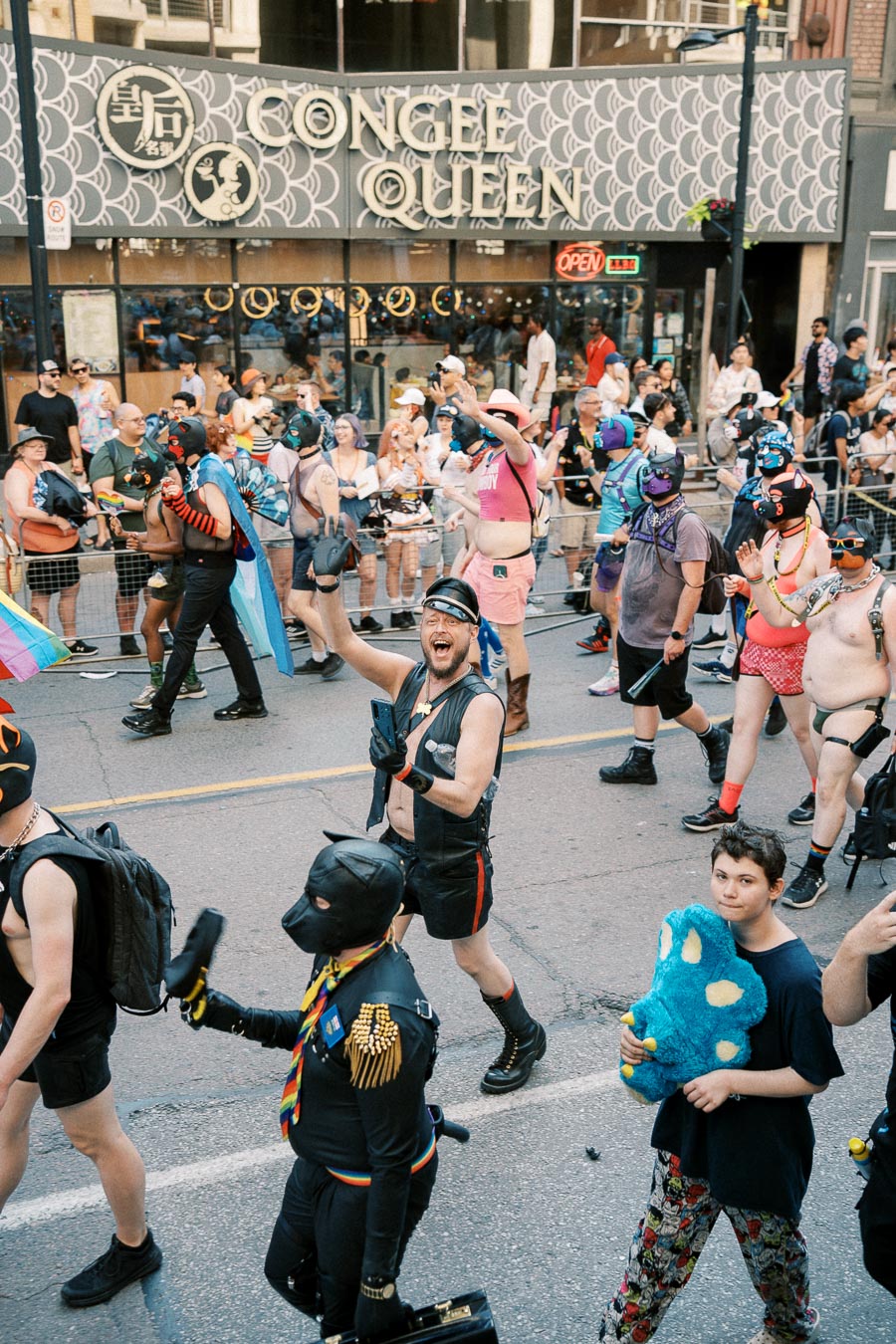 Participants in vibrant costumes parade past Congee Queen, engaging with spectators during a lively street event.