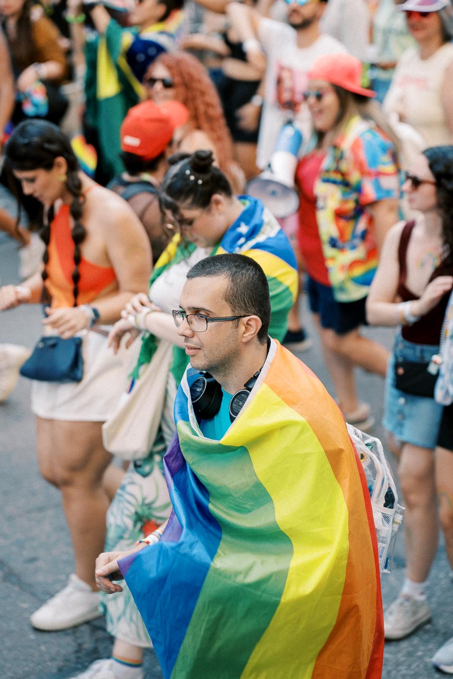 Participants at a pride parade, with one individual prominently wearing a rainbow flag as a cape, symbolizing LGBTQ+ pride.