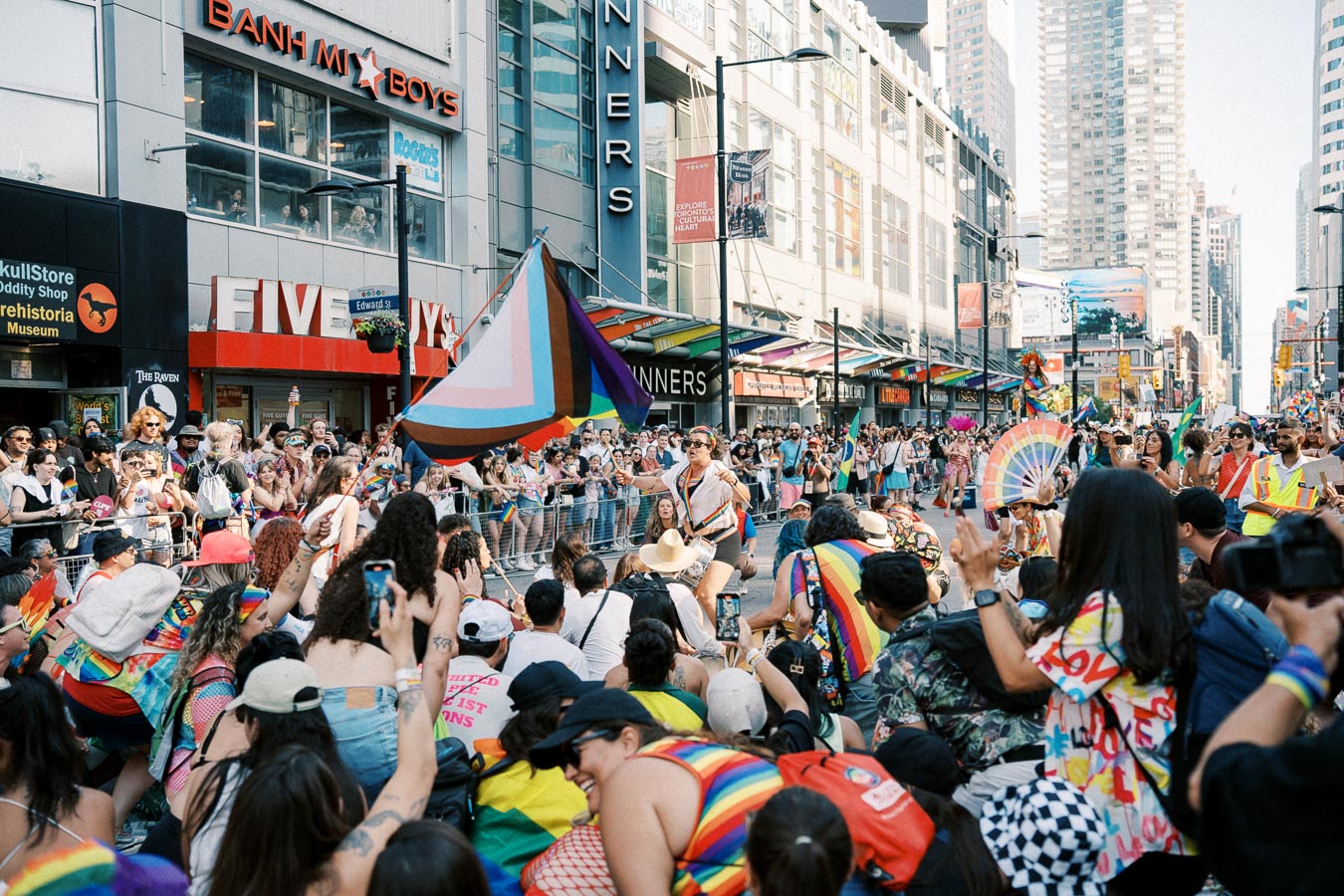 A lively pride parade with participants and spectators celebrating with colorful flags and outfits in an urban setting.