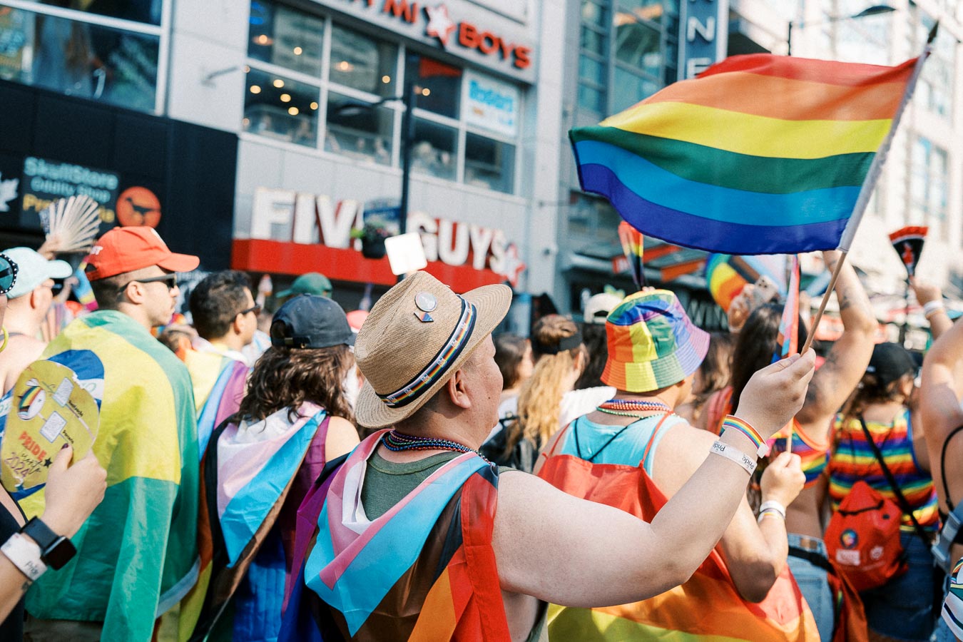 Participants at a Pride parade celebrate with rainbow flags and colorful attire, showcasing support for the LGBTQ+ community.