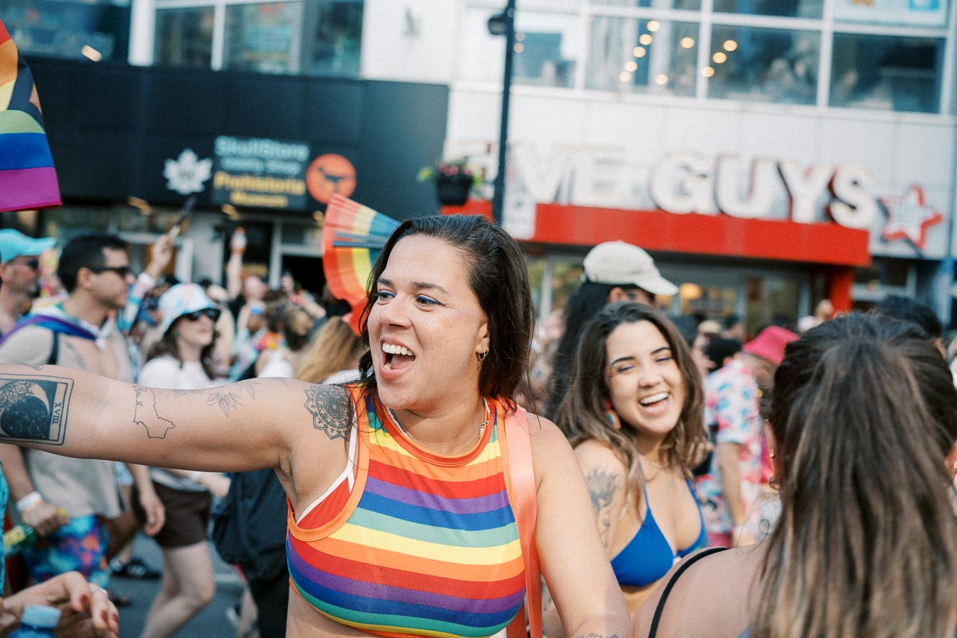 Participants joyfully celebrate at a pride parade, wearing colorful rainbow attire and smiling amidst a lively crowd.