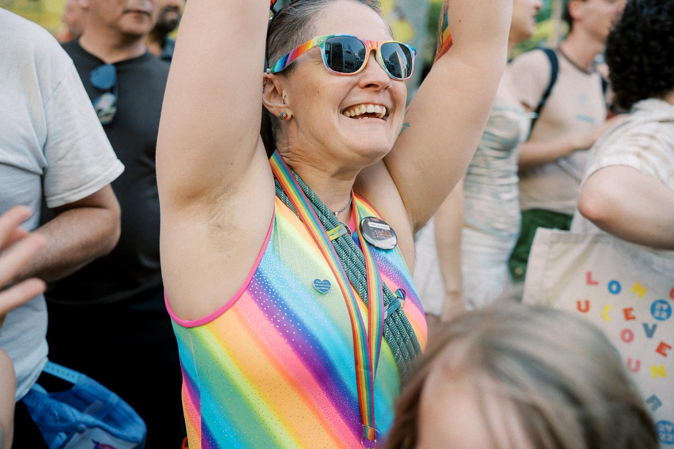 A joyful participant at a pride event, wearing rainbow-themed attire and accessories, celebrates with the crowd.