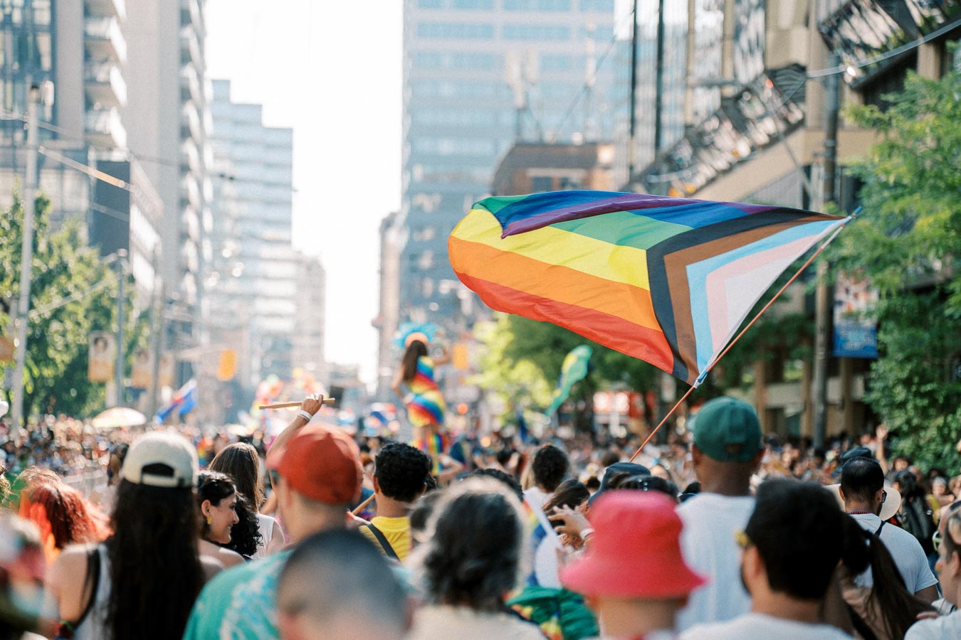 A lively scene from a Pride parade, featuring a diverse crowd and a prominent rainbow flag symbolizing inclusivity.
