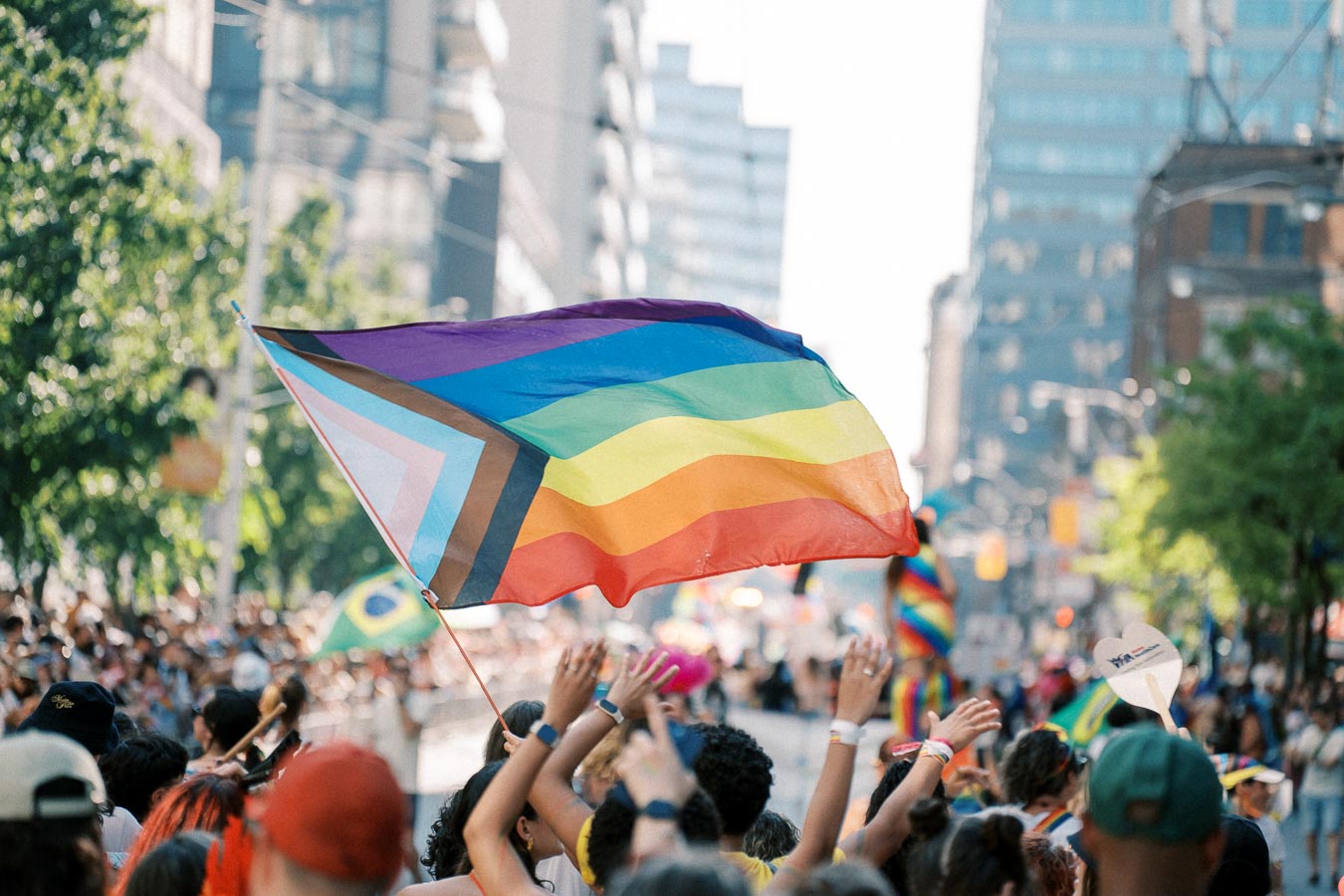 A vibrant pride parade with participants waving a rainbow flag featuring additional colors for inclusivity.