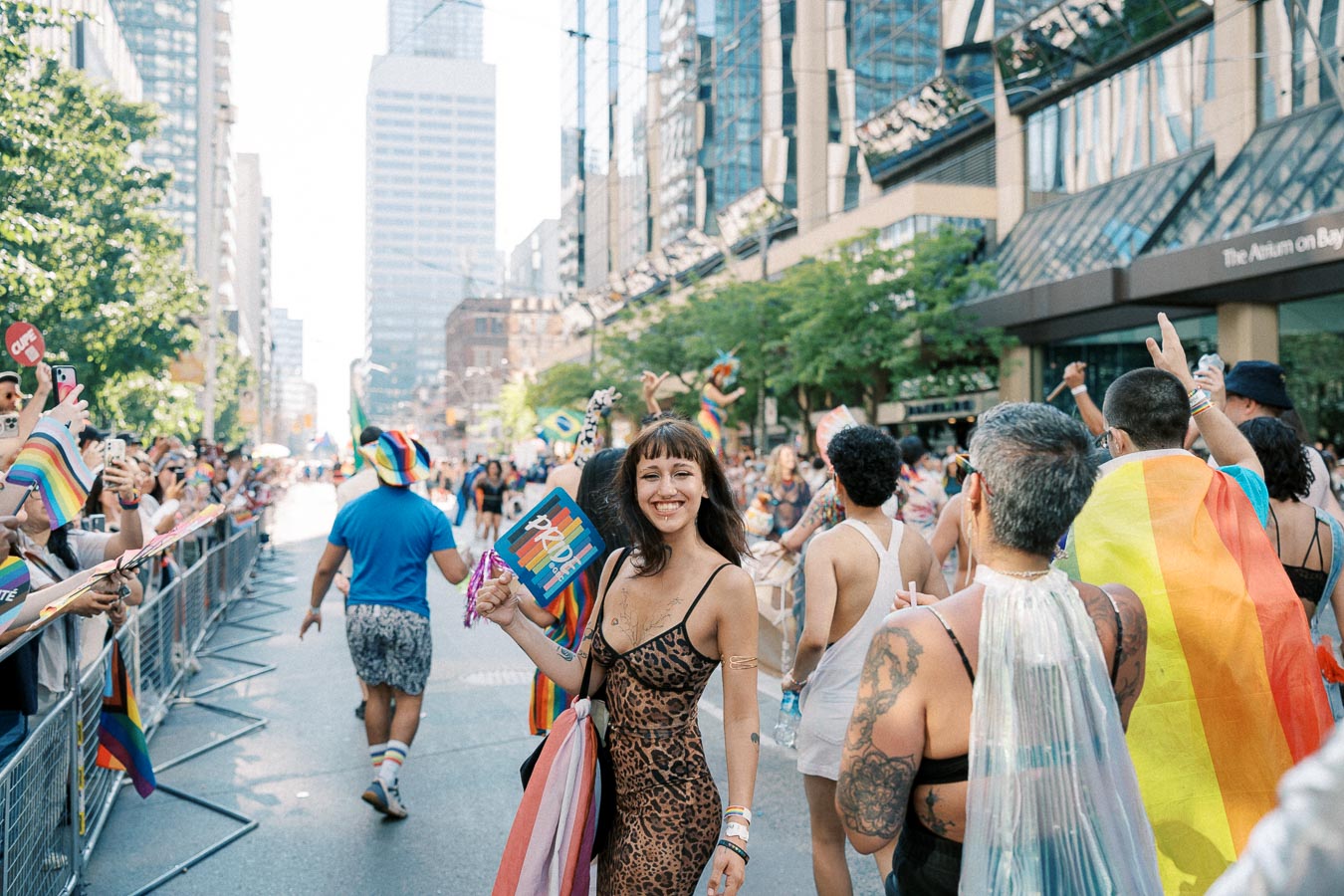 Participants celebrate at a vibrant Pride parade, showcasing colorful outfits and rainbow flags amidst a bustling city street.