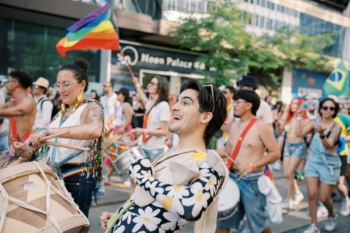 Participants joyfully play drums and wave a rainbow flag during a vibrant parade.
