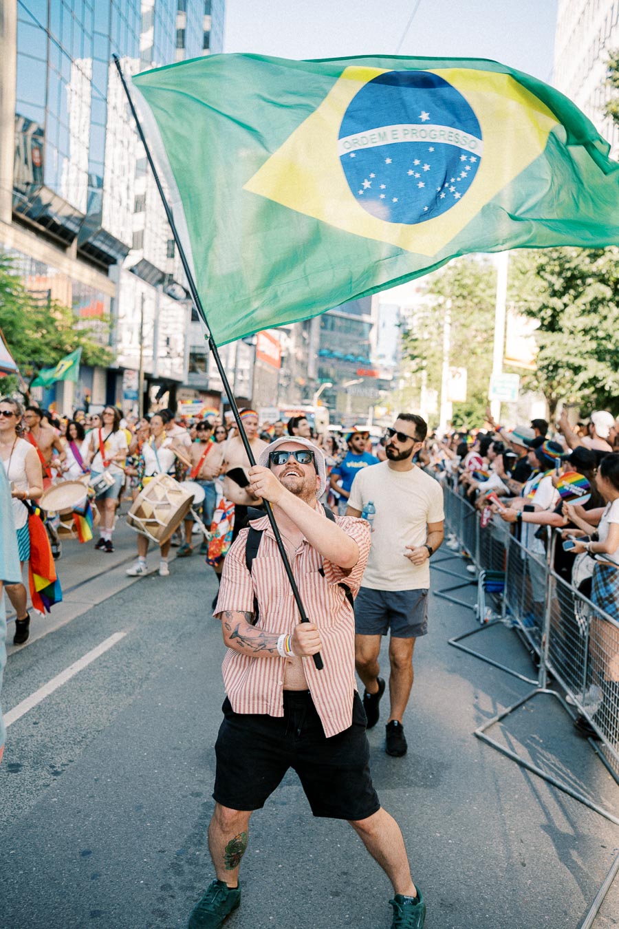 A participant waves a Brazilian flag at a lively street parade, surrounded by a festive crowd.