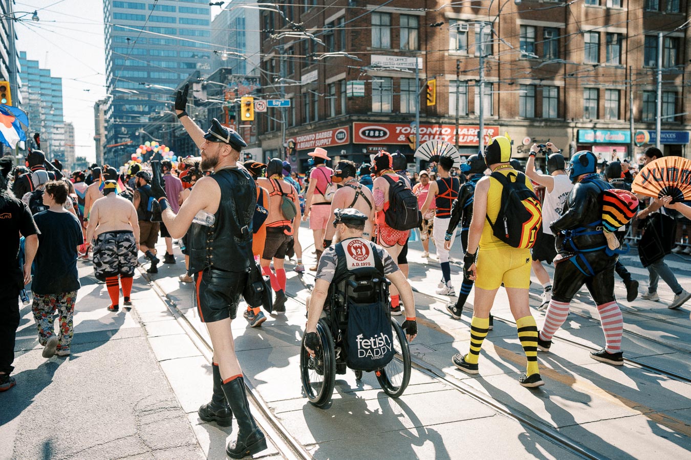 Participants in colorful costumes march in a city parade, showcasing diverse expressions and styles.