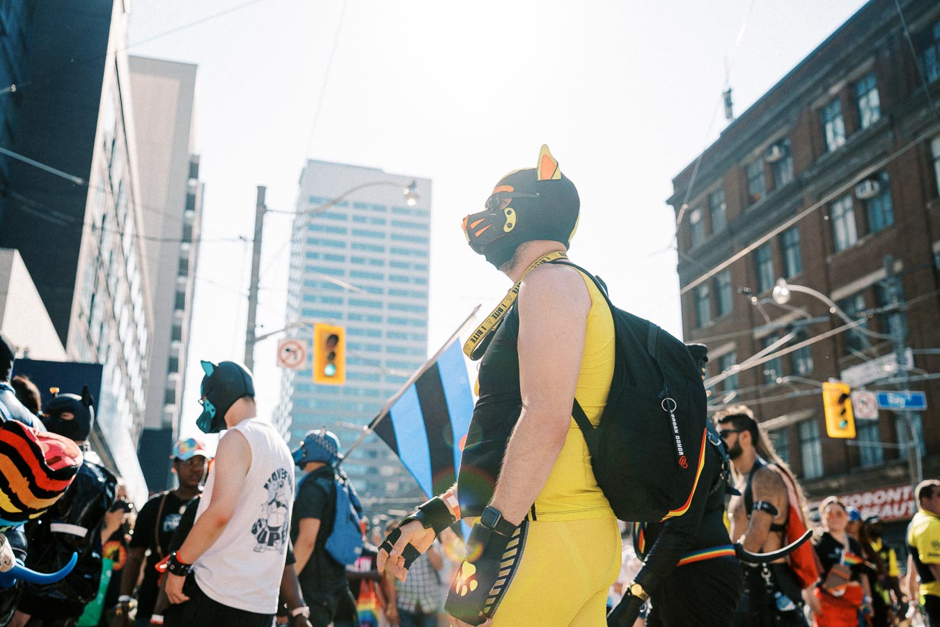 Participants in colorful costumes and masks take part in a lively street parade, set against the backdrop of urban buildings.