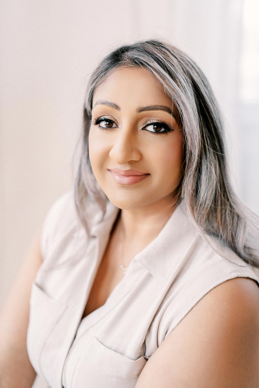 A woman with long hair and a light-colored sleeveless top smiles warmly at the camera.