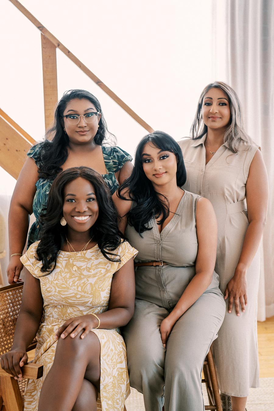 A group of four women smiling and posing together indoors, showcasing a sense of friendship and style.
