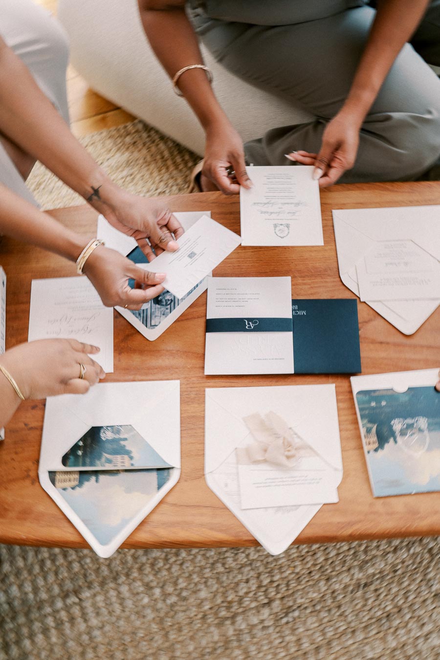 A group of people sorting through a collection of elegant invitation cards on a wooden table, with some cards featuring decorative elements like ribbons and embossed text.