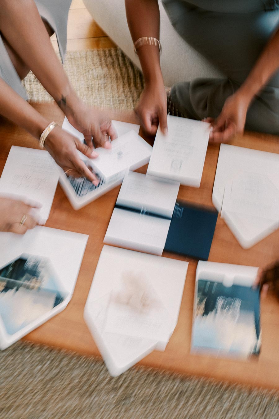 A group of people sorting through various paper documents on a wooden table. The image is blurred, making it difficult to discern specific details of the documents.