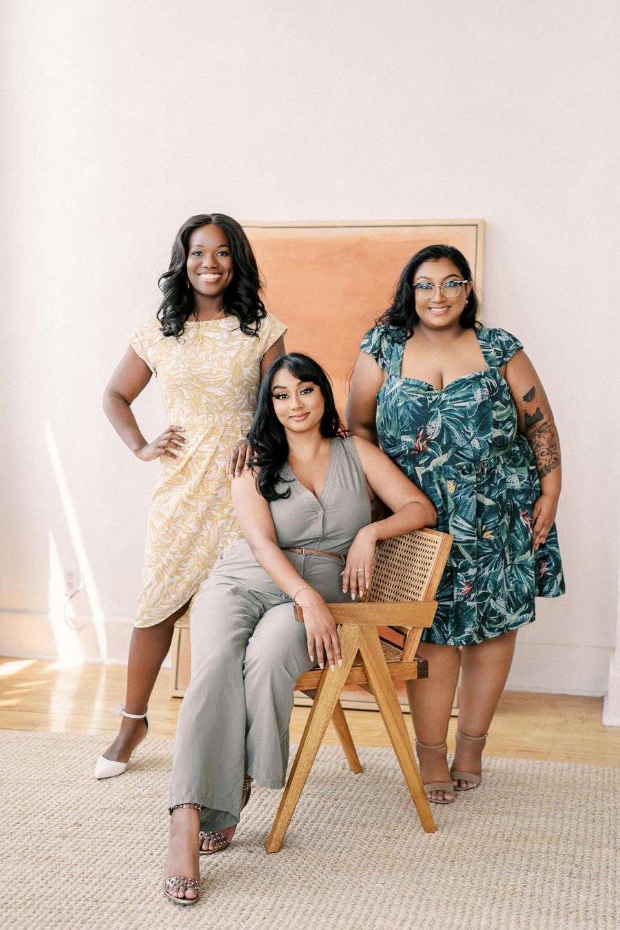 Three women pose together in a bright, stylish setting, showcasing their fashionable outfits and confident smiles.