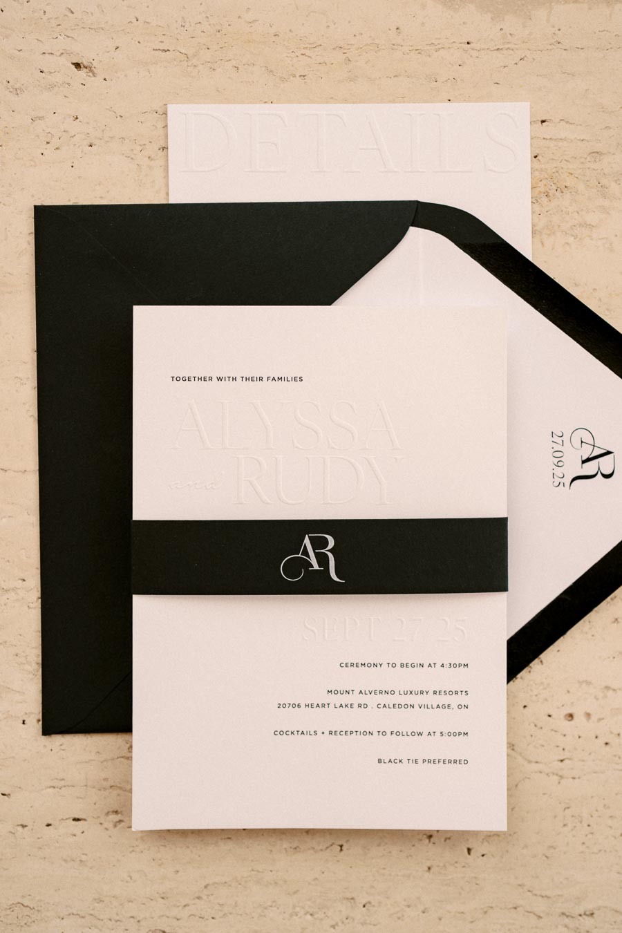 A sophisticated wedding invitation set featuring a black and white theme with embossed text. The invitation includes a black band with the initials 'AR' and details about the ceremony at Mount Alverno Luxury Resorts.