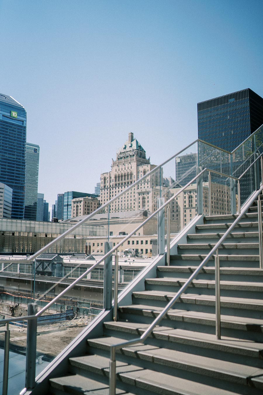 Modern cityscape with glass rail stairway and high-rise buildings under a clear blue sky.
