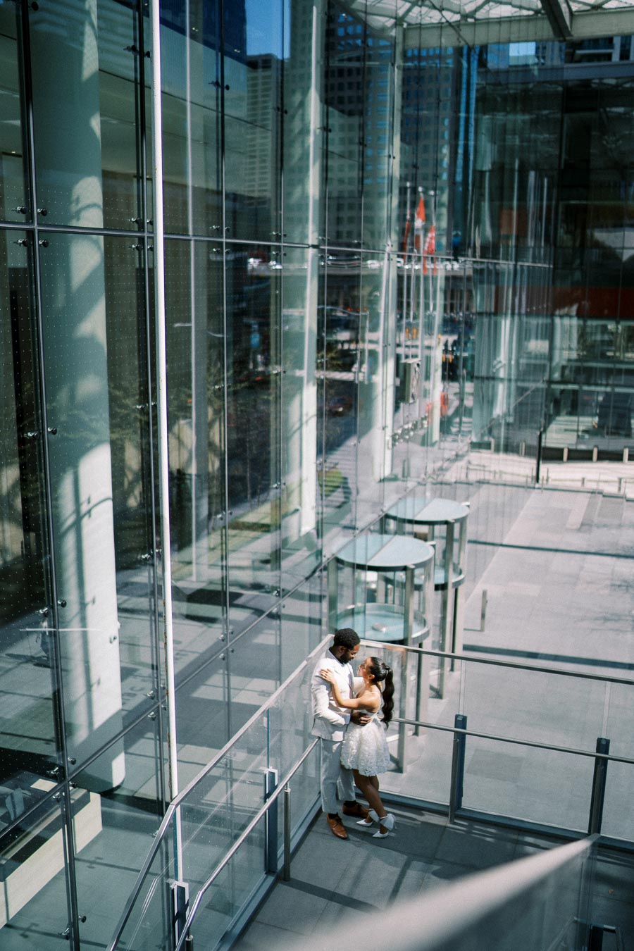 A couple embracing in a modern glass building with cityscape reflections, showcasing urban romance and architectural design.