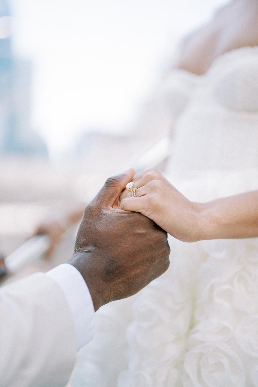 A close-up of a couple holding hands during a wedding ceremony, with the focus on the bride's engagement ring and wedding band.
