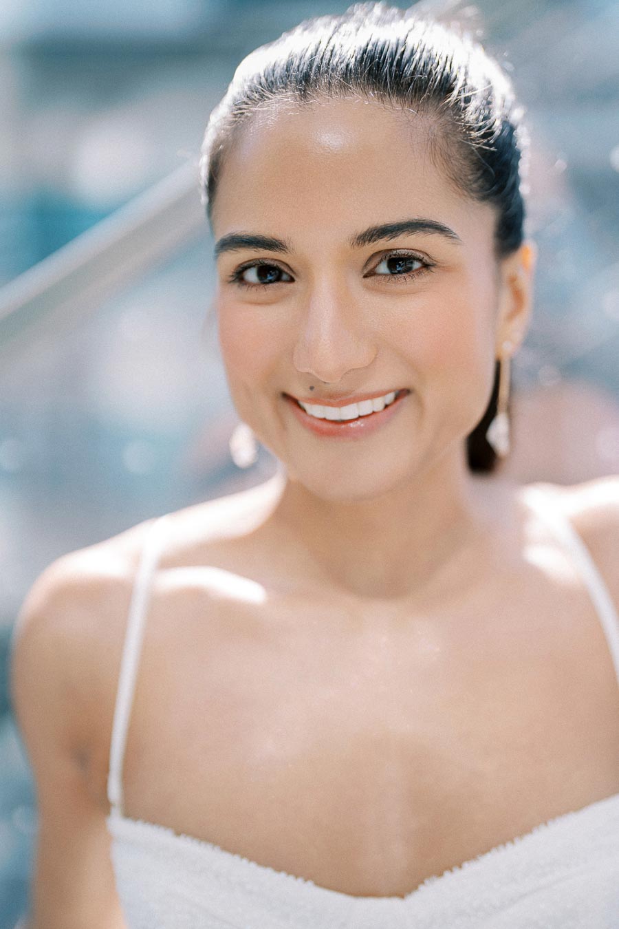 Young woman with a radiant smile and glowing skin, wearing a white top, in a bright and softly blurred background.
