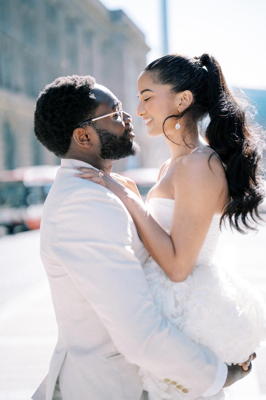 A joyful couple in wedding attire sharing a romantic moment outdoors, with the groom in a light suit and the bride in a strapless white dress.