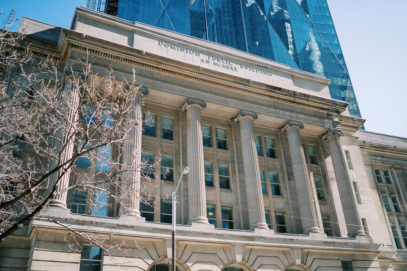Historic Dominion Public Building with classical columns under a clear blue sky in an urban setting, capturing architectural details and modern glass structures in the background.